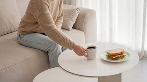A person sitting on a sofa with a plate of sandwich and a cup of coffee on a small table. - Pohang Baritdol Pension (Pohang)