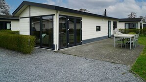 Ein modernes Gebäude mit Flachdach, großen Glasfenstern und einer Terrasse mit Tisch und Stühlen.