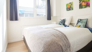 Ein Schlafzimmer mit Bett, Fenster, Vorhängen und Wandbildern.