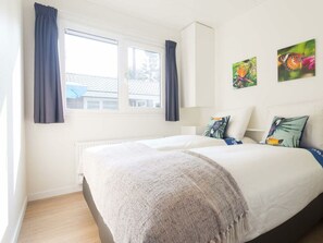Ein Schlafzimmer mit Bett, Fenster, Vorhängen und Wandbildern.