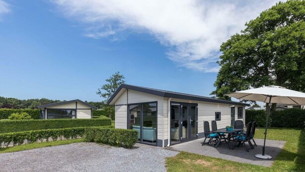 Ein modernes Haus mit Terrasse, einem Essbereich mit Stühlen und Tisch sowie einer überdachten Sitzgelegenheit im Freien.