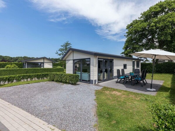 Ein modernes Haus mit Terrasse, einem Essbereich mit Stühlen und Tisch sowie einer überdachten Sitzgelegenheit im Freien.