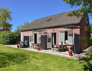 Ein Backsteinhaus mit einer Terrasse, die Sitzgelegenheiten, einen Tisch und einen überdachten Bereich mit Sonnenschirm bietet.