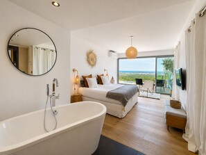 A modern bedroom with a large bathtub, a bed with multiple pillows, a round mirror, and a view of the outdoors. - Panoramic sea view house with private jacuzzi between Antibes and Cannes (Vallauris)