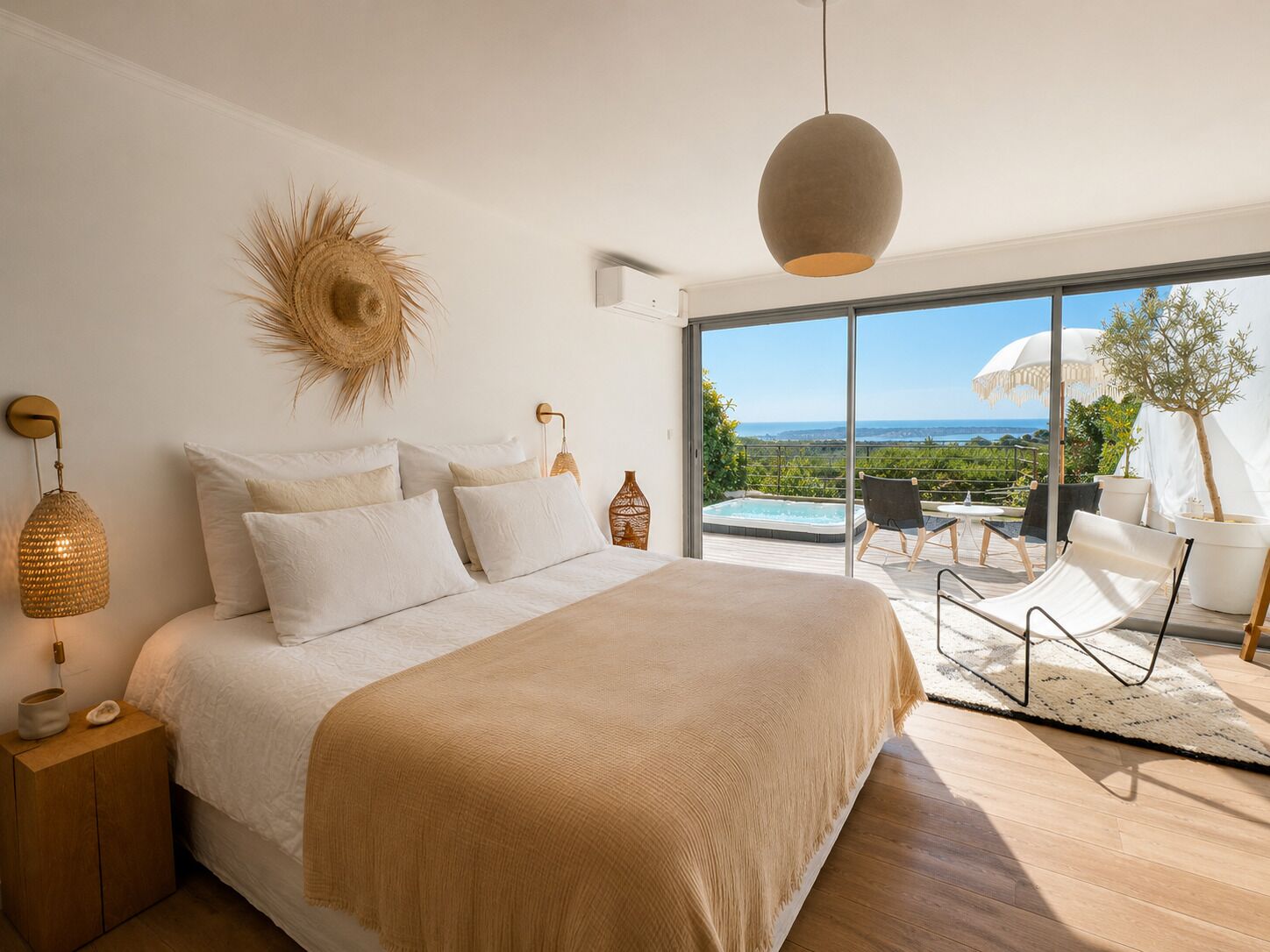 A bedroom with a large bed, a view of the outdoors, and a balcony with seating.