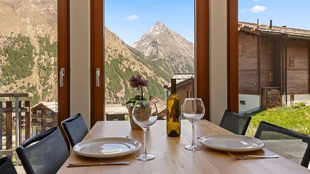 Una mesa de comedor con platos, copas de vino y una botella, con vistas a la montaña.