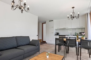 Ein modernes Wohnzimmer mit einer Couch, einem Esstisch, Stühlen und einer Küche im Hintergrund.