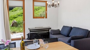 Una sala de estar con un sofá, una mesa de comedor con copas de vino y platos, un teclado y vistas a zonas verdes al exterior.