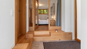 Un pasillo que conduce a un dormitorio con cama, mesita de noche y ventana con cortinas.