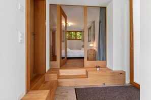 Ein Flur, der in ein Schlafzimmer mit Bett, Nachttisch und einem fenster mit Vorhängen führt.