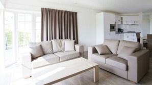 Ein modernes Wohnzimmer mit zwei Sofas, einem Couchtisch und einer Küche im Hintergrund.