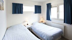 Ein Zimmer mit zwei Betten, einem fensterbelaubten Fenster, einem Heizkörper und einer Wandlampe.