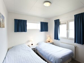 A room with two beds, a window with curtains, a radiator, and a wall-mounted lamp. - Holiday Home in Breskens With Terrace (Breskens)