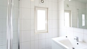 Ein Badezimmer mit weißen Fliesen, einem Waschbecken, einem Spiegel und einem Fenster.