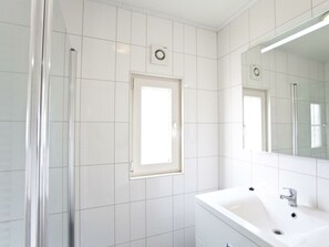 A bathroom with white tiles, a sink, a mirror, and a window. - Holiday Home in Breskens With Terrace (Breskens)