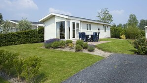 Ein Bungalow mit Terrasse, einem kleinen Garten und einem Einfahrt mit Kies.