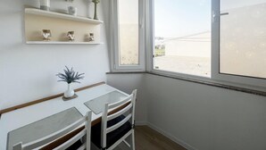 Quarto com uma mesa e cadeiras, uma janela com vista e estantes com objetos decorativos.