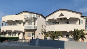 Um edifício residencial de dois andares com varandas, portão fechado e palmeiras.