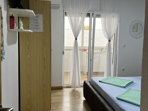 A hotel room with a bed, a wooden door, a window with sheer curtains, a view of the balcony, and a wall clock. - Apartment Lavaran 5 (Vir)