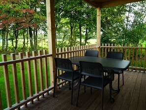 Eine überdachte Terrasse im Freien mit Tisch und Stühlen, umgeben von einem Holzzaun und Bäumen.