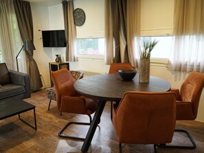 Ein modernes Wohnzimmer mit einem runden Tisch, Ledersesseln, einem Flachbildfernseher und einer Wanduhr.