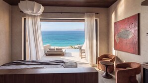 A bedroom with a bed, a chair, a table, and a view of the ocean. - Lofos Social House (Hersonissos)
