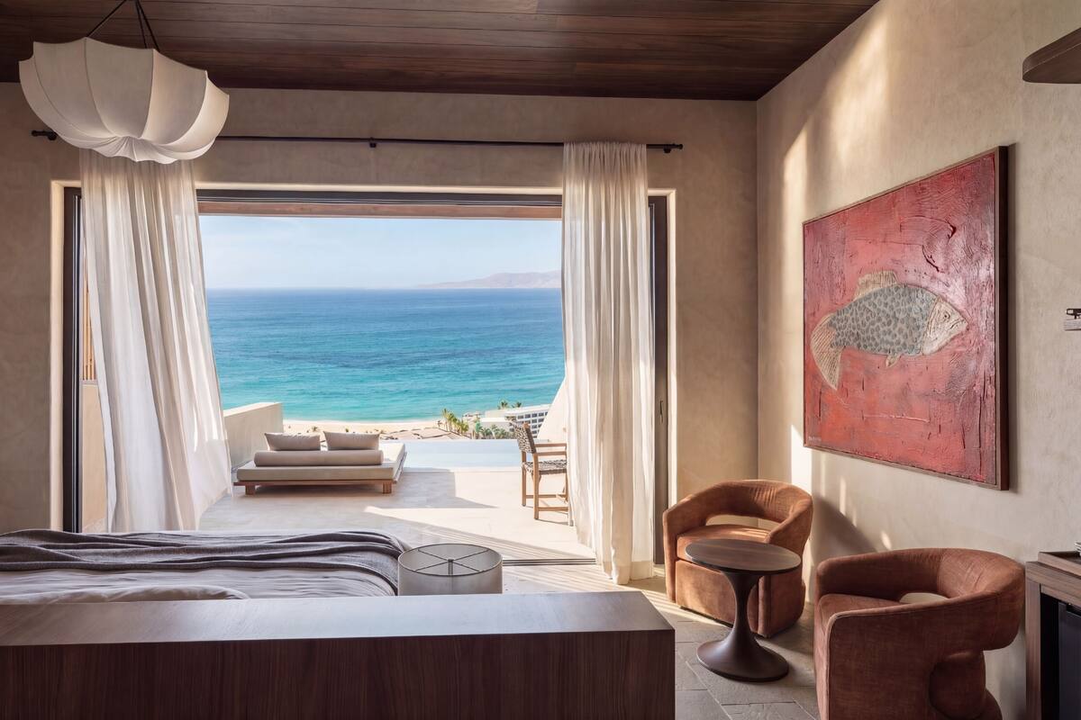 A bedroom with a bed, a chair, a table, and a view of the ocean.