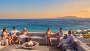 A group of people seated on outdoor sofas with a fire pit, overlooking a coastal view. - Lofos Social House (Hersonissos)