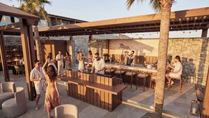 An outdoor bar area with a wooden bar, seating, and a stone wall backdrop. - Lofos Social House (Hersonissos)