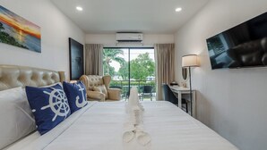 A hotel room with a bed, a TV, a chair, and a view of greenery outside. - Beachside 1BR•Walk to Rawai•Cozy-title rawai C201 (ตำบล ราไวย์)