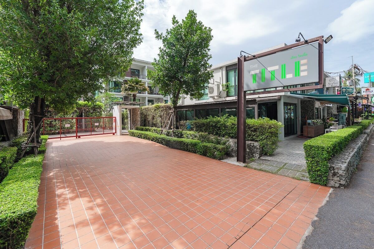 A hotel entrance with a tiled pathway, a red gate, and greenery.