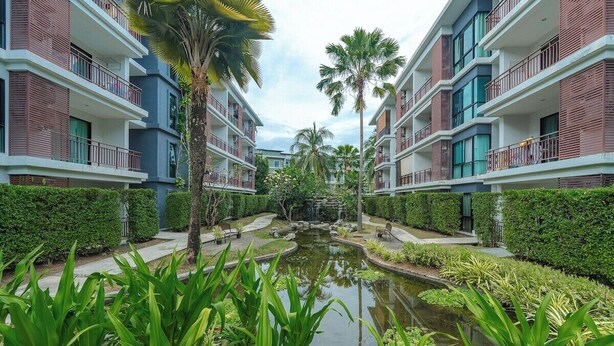 A modern hotel with multiple floors, a central courtyard with a pond, and surrounding greenery. - Beachside 1BR•Walk to Rawai•Cozy-title rawai C201 (ตำบล ราไวย์)