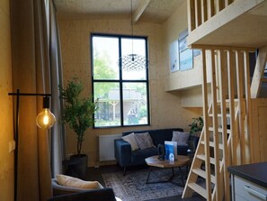 A cozy room with a large window, a blue sofa, a wooden ladder, and a small table with a plant. - Holiday Home in Warmond With Terrace (Warmond)