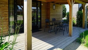 A wooden deck with a table and chairs, a covered area with a hanging light fixture, and a glass door leading to a garden. - Holiday Home in Warmond With Terrace (Warmond)