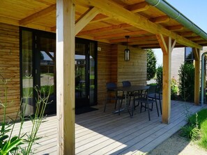 A wooden deck with a table and chairs, a covered area with a hanging light fixture, and a glass door leading to a garden. - Holiday Home in Warmond With Terrace (Warmond)