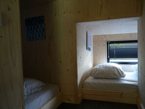 A small, wooden room with two beds, a window with blinds, and a blue abstract painting on the wall. - Holiday Home in Warmond With Terrace (Warmond)