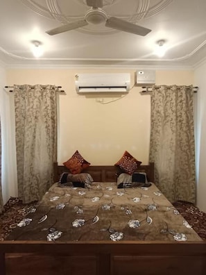A bedroom with a bed, two pillows, a ceiling fan, and an air conditioning unit. - P&Q GUEST HOUSE (Budgam)