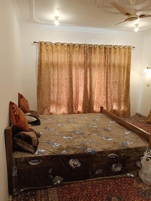Quarto com cama, cortinas, almofadas, ventilador de teto e tapete.