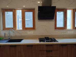 A kitchen with two windows, a sink, a stove, and a wall-mounted TV. - P&Q GUEST HOUSE (Budgam)