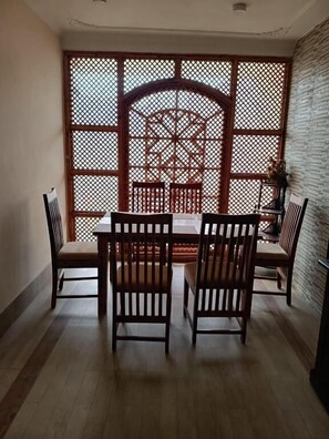 Uma área de refeições com uma mesa e cadeiras de madeira, um biombo decorativo e uma parede de tijolos.