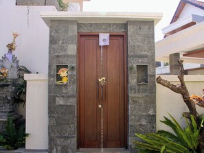 Una puerta de madera con una placa decorativa, flanqueada por muros de piedra y pequeñas ventanas.