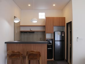 A modern kitchen with wooden cabinets, a stainless steel refrigerator, two bar stools, pendant lights, and a window. - Mimpi Ayung Villas by AGATA (Badung)