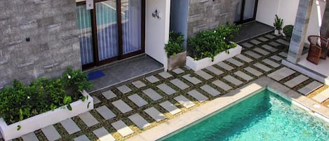 A modern outdoor pool area with a stone pathway, potted plants, and a clear blue pool.