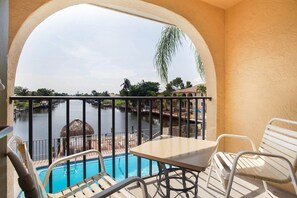 Un balcón con piscina, sillas y vistas a un cuerpo de agua y edificios.