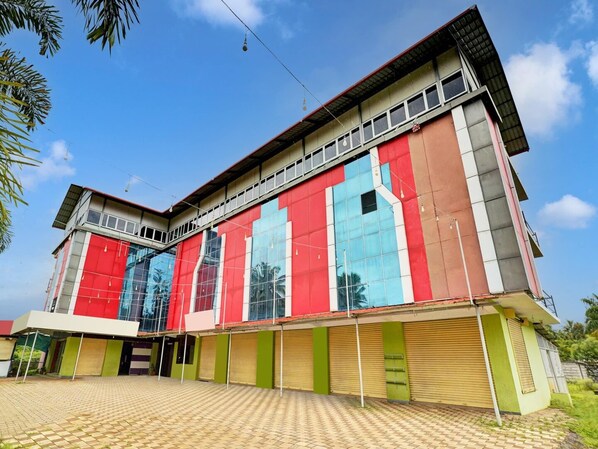 A multi-story building with a red and blue facade, large windows, and a tiled ground floor. - Deluxe Collection O Coorg Arvind Premium (Somvarpet)