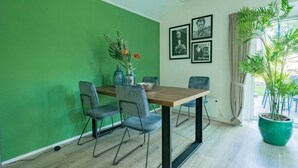 A dining area with a green wall, a wooden table, and four chairs. There are framed pictures on the wall and a potted plant near the window. - Holiday Home in Maarn With Terrace (Maarn)