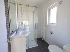 Ein Badezimmer mit Glasdusche, Waschbecken, Toilette und Fenster.