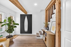 Interior moderno com vigas de madeira, uma escada, um vaso com planta e uma grande obra de arte preta.