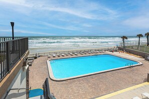 Ein Pool mit Blick auf den Ozean, einer Pflasterterrasse und einer Brüstung.