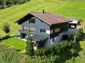 A modern two-story house with a sloped roof, a covered outdoor area, and a car parked in a garage.